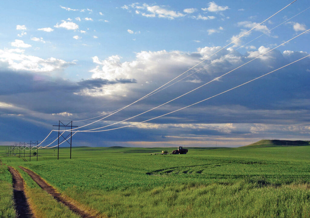 Power lines in Upper Great Plains region suspended over green fields.