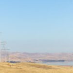 A transmission line in Sierra Nevada Region stretches across steel monopole structures shown in foreground with the San Luis, Reservoir in the distance.