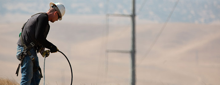 A lineman in the field working with a de-energized powerline at ground level.
