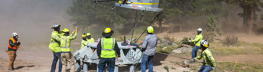 Team leader and a team of eight positioning a powerline tower suspended from a helicopter into position on the tower base.